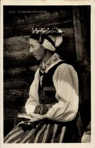 Ak Evolène Kanton Wallis, Eine junge Frau in Tracht steht vor einer Holzwand.