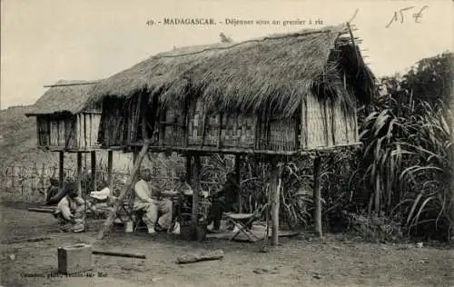 Ak Madagaskar Madagascar, Drei traditionelle strohgedeckte Speicher, Personen bei einem Essen