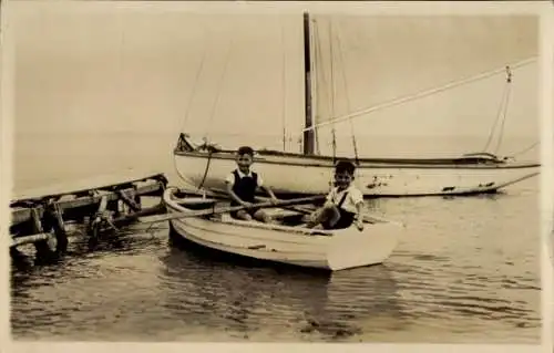 Ak Ostseebad Timmendorfer Strand, Junge auf einem Boot, Segelboot im Hintergrund, ruhige Wasserob