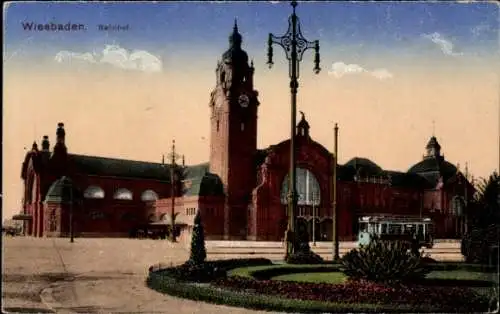 Ak Wiesbaden in Hessen, Bahnhof, rote Backsteinarchitektur, Uhrturm, Straßenbahn, Parkanlage