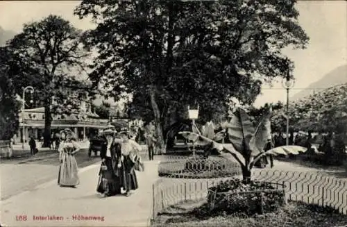Ak Interlaken Kanton Bern Schweiz, Vordere Ansicht: Bäume, Straße, Menschen in Tracht, Pflanzen, 