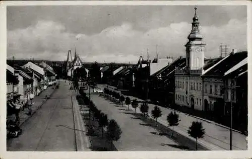 Ak Rakovnik Rakonitz Mittelböhmen, Straße mit Bäumen, Häusern, Kirchturm, Schwarz-Weiß-Foto