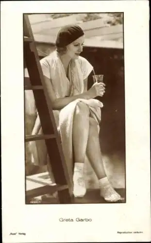 Ak Schauspielerin Greta Garbo, Sitzportrait, Mütze, Glas