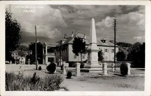 Ak Цетиње Cetinje Montenegro, Obelisk, Gebäude im Hintergrund, Parkähnliche Umgebung, Wolkenhimme