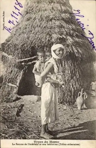Ak Marokko, Eine Frau mit einem Kind auf dem Rücken steht vor einer Hütte.
