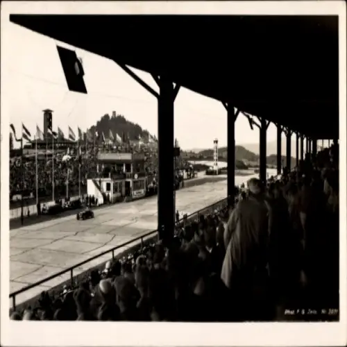 Ak Nürburg in der Eifel, Nürburgring, Rennauto, Zuschauertribüne, Flaggen, Nürburg im Hintergrund