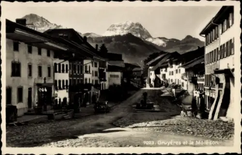 Ak Gruyères Kanton Freiburg Schweiz, Straße mit Gebäuden, Bergen im Hintergrund, Brunnen