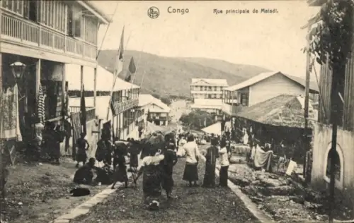 Ak Matadi DR Kongo Zaire, Hauptstraße, Menschen, Geschäfte, Flaggen, Berge im Hintergrund
