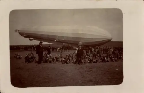 Foto Ak Zeppelin Luftschiff über einem Flugfeld, Schaulustige, aufgestellte Gewehre und Pickelhauben