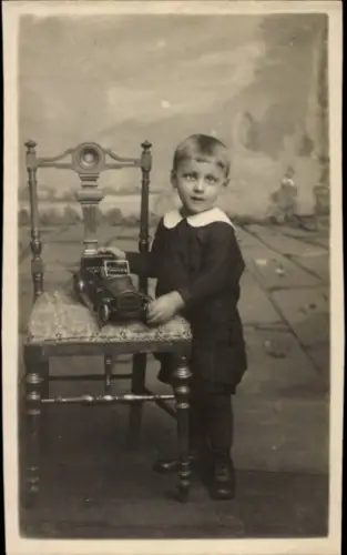 Foto Ak Kinderportrait, kleiner Junge mit einem Spielzeugauto, Stuhl