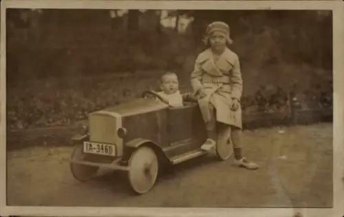 Foto Ak Kinderportrait, Mädchen im Mantel, Kleinkind sitzt in einem Spielzeugauto