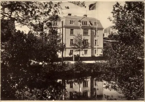 Ak Ronneby Schweden, Gebäude mit Flagge, Wasserreflexion, Bäume im Vordergrund