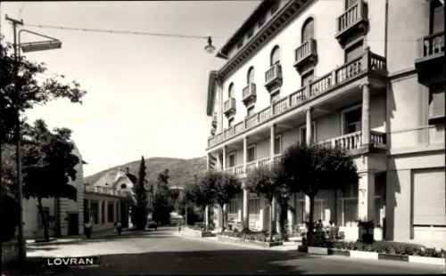 Ak Lovran Laurana Kroatien, Straße in  Gebäude mit Balkonen, Bäume, keine Personen sichtbar