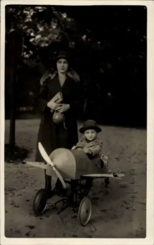 Foto Ak Kleinkind in einem Flugzeug auf Rädern, Frau im Mantel