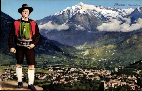 Ak Meran Merano Südtirol, Mann in Tracht, Berglandschaft, Stadt Merano im Hintergrund, Schneeberg