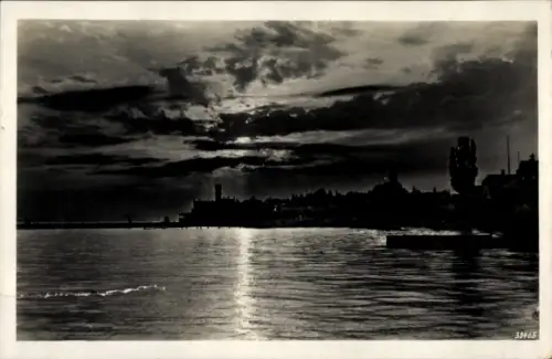 Ak Langenargen am Bodensee, Dunkler Himmel, Wasseroberfläche, Silhouette von Bäumen und Gebäuden