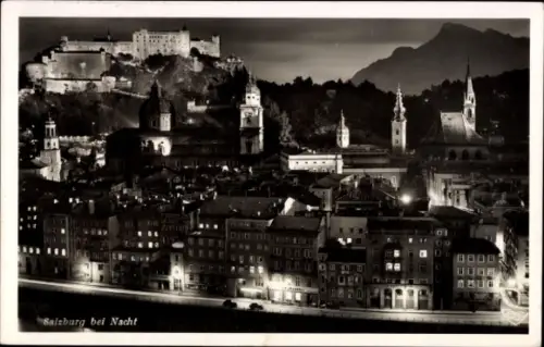 Ak Salzburg in Österreich, Salzburg bei Nacht, beleuchtete Stadt, Festung, Berge im Hintergrund