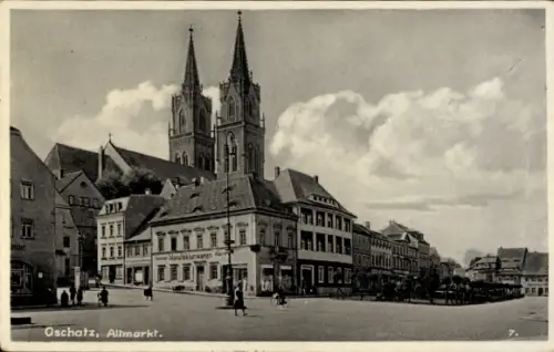 Ak Oschatz in Sachsen, Zwei spitze Kirchtürme, Reihenhäuser mit Ladengeschäften, Passanten auf of