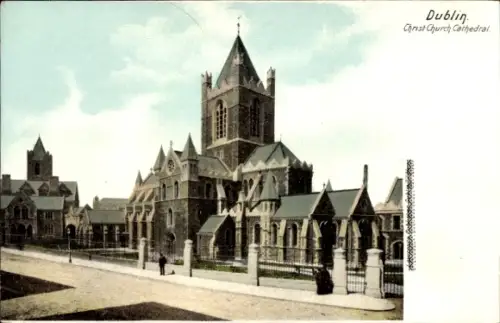 Ak Dublin Irland, Kathedrale mit hohem Turm, Nebengebäude, Metallzaun, Gehweg, zwei Personen
