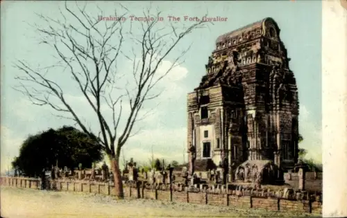 Ak Gwalior Indien, Hindutempel mit hohem Turm, kahler Baum im Vordergrund, Steinmauer und Grabste