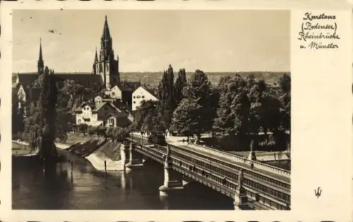 Ak Konstanz am Bodensee, Brücke über Fluss, hoher Kirchturm, Wohnhäuser am Ufer, Baumreihe/Promen