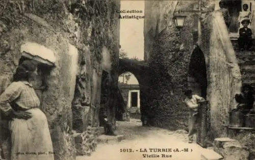 Ak La Turbie Alpes Maritimes, Enge Gasse, Torbogen, Lampe, Frau mit Hut links, Person mit Besen r