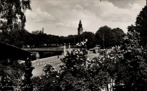 Ak Turku Åbo Finnland, Flussuferpromenade, Brücke, Uferbepflanzung mit Büschen, hoher Turm im Hin
