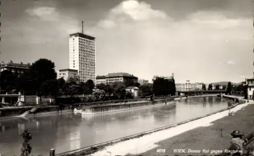 Ak Wien 1 Innere Stadt, Flusskanal, hoher Turm, Uferweg mit Gehweg, Bäume, Brücke im Hintergrund,