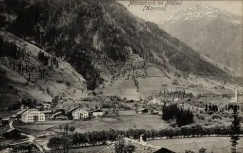 Ak Mörtschach in Kärnten, Dorf mit Häusern, Kirchturm, Wiesen/Felder, Baumreihe, bewaldete Hänge,