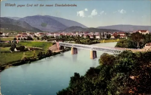 Ak Villach in Kärnten, Fluss mit Eisenbahnbrücke, Uferwiesen, Bäume, Hügel im Hintergrund