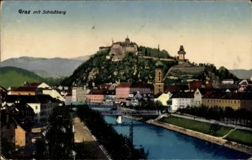 Ak Graz Steiermark, Fluss mit Brücke, Häuserzeilen am Ufer, hoher bewaldeter Hügel mit Turm