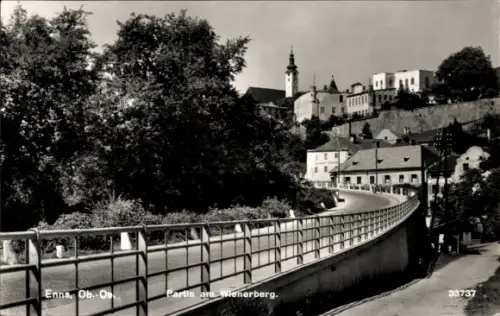 Ak Enns in Oberösterreich, gekrümmte Straße mit Geländer, große Bäume links, Häuser am Hang, sich