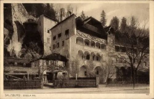 Ak Salzburg in Österreich, Mehrstöckiges Haus mit Arkaden, Felsenwand im Hintergrund, Zaun und St