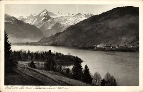 Ak Zell am See in Salzburg, See, Ufer mit Bäumen und Wiesen, Hangweg, Dorf gegenüber, schneebedec