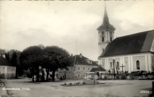 Ak Aistersheim Oberösterreich, Kirchturm mit Kirchenschiff, Friedhofskreuze, große Bäume am Platz