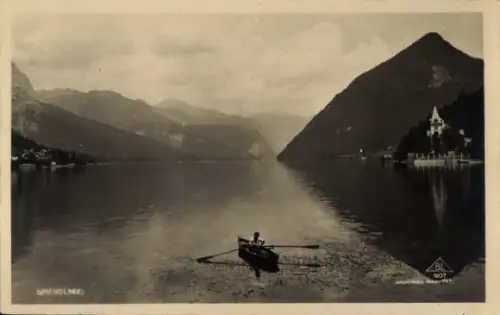 Ak Grundlsee Steiermark, Ruderboot mit Person auf See, Berge im Hintergrund, Gebäude am rechten U