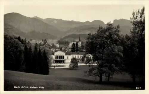 Ak Bad Ischl in Oberösterreich, Gebäude mit Portikus, Wiese vorne, Bäume und Wald, Kirchturm, Ber