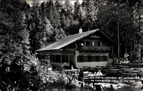 Ak Oetz in Tirol, Holz-Alpenhaus mit Balkon, Außenterrasse mit Bänken und Tischen, dichter Nadelw