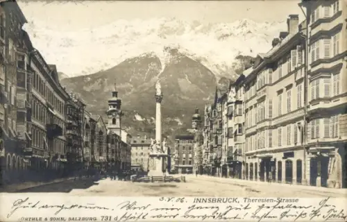 Ak Innsbruck in Tirol, Säulenstatue in Straßenmitte, schneebedeckte Berge, Häuser beidseits, Fußg