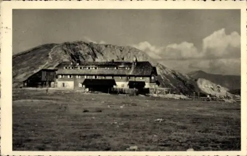 Ak Bergmassiv Rax Niederösterreich, Längliches Berghaus vor Felswand, weite Wiese im Vordergrund,