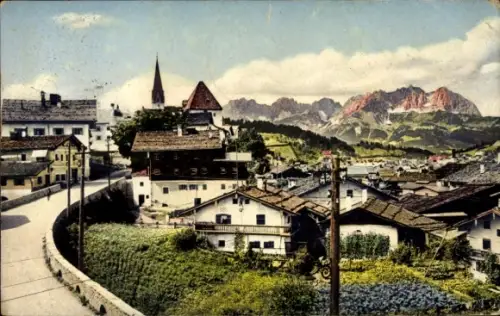 Ak Kitzbühel in Tirol, Kirchturm, Häuserdächer, gewundene Straße, Gärten, Strommast, Alpenkette i