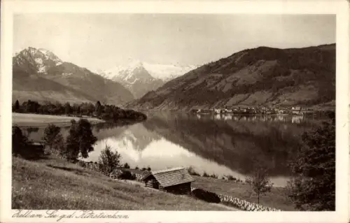 Ak Zell am See in Salzburg, See mit Spiegelung, schneebedeckte Gipfel, Uferwiese mit Bäumen, Holz