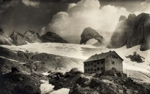 Ak Gosau in Oberösterreich, Adamekhütte, Steinhaus-Hütte auf felsigem Vorsprung, Gletscherfeld da