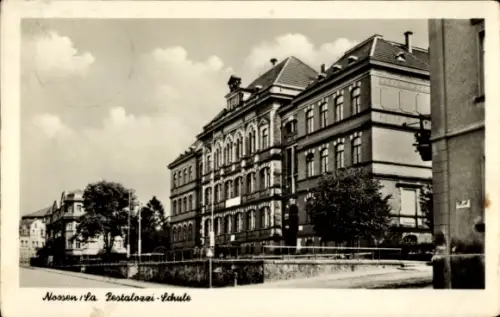 Ak Nossen in Sachsen, Mehrstöckiges Schulgebäude, Zaun und Vorgarten, Gehweg, Bäume, Wolken