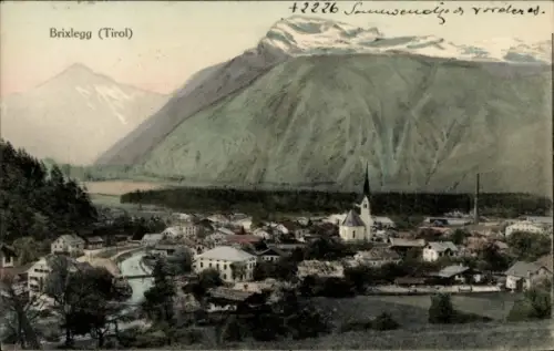 Ak Brixlegg in Tirol,  Dorfansicht, Pfarrkirche mit spitzem Turm, Brücke über Fluss, Alpenberge