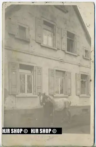 Mann und Pferd vor einem Haus
