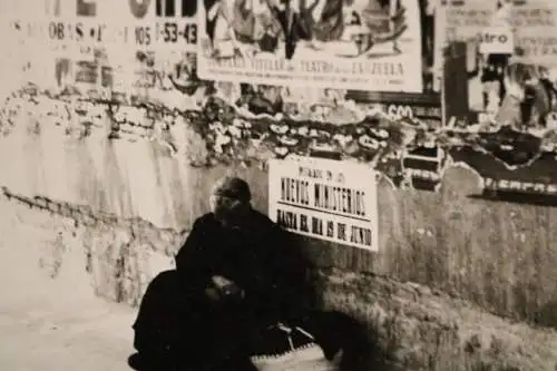 altes Foto - alte Frau sitzt an Mauer mit Plakaten - Spanien ??