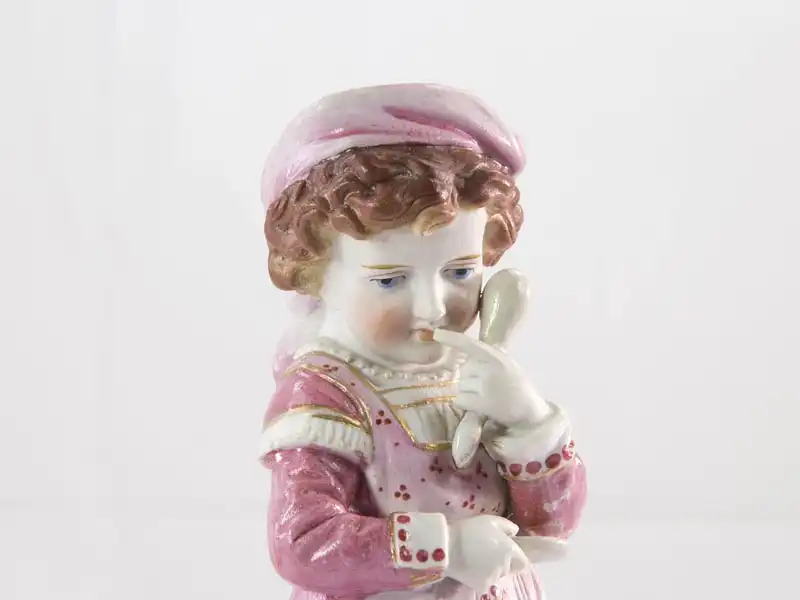 Porzellanfigur,
Ende 19. Jh., wohl Thüringen, Mädchen mit Löffel und Schüssel in der Hand, zartrosa bemalt, originelle Ausformung, an Löffel und Schüssel Restaurierungen, sonst unbeschädigt.
 1