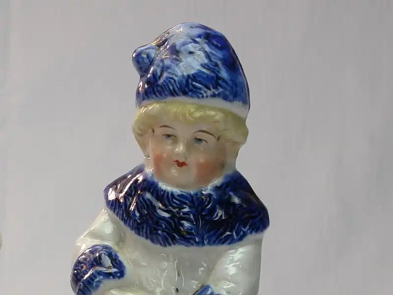 Paar Porzellanfiguren, um 1900, ungemarkt, Mädchen und Junge in Wintersachen, blau-weiß bemalt, im Fuß des Mädchens Brandrisse, sonst unbeschädigt. H: 22 cm 2