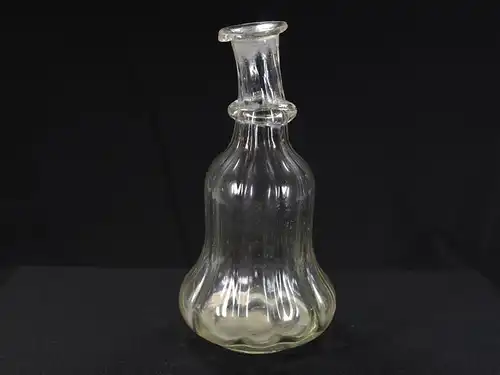 Glasflasche, 18. Jh., leicht gelblstichiches Glas, glockenförmiger Körper spiralförmig gedreht mit Abriß, schräger Hals mit angesetzten Glasknoten. H: 17 cm